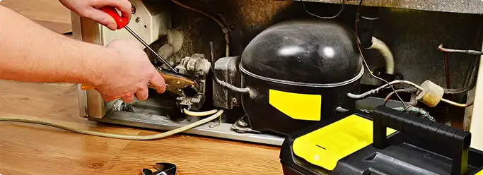 Refrigerator repair technician fixing the compressor and wiring in Emmaus, PA