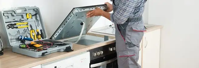 Cooktop repair technician lifting a built-in stovetop for service in Allentown, PA