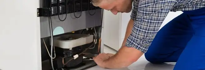 Refrigerator repair technician servicing the compressor and condenser area in Allentown, PA