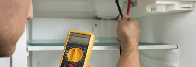 Refrigerator repair technician testing electrical components with a multimeter in Allentown, PA